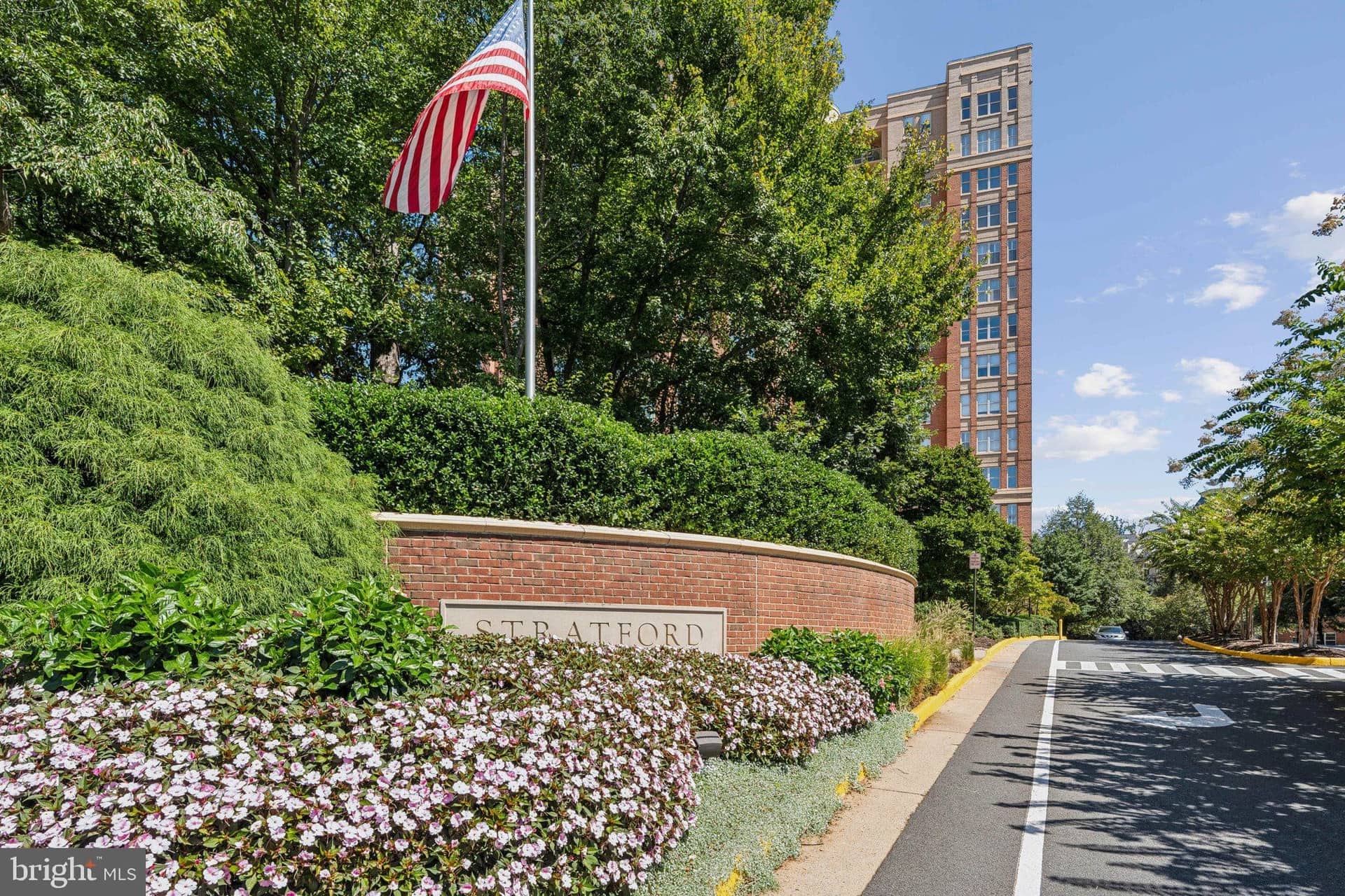 Landscaped Stratford House arrival drive with its monument sign, American flag, and high-rise tower