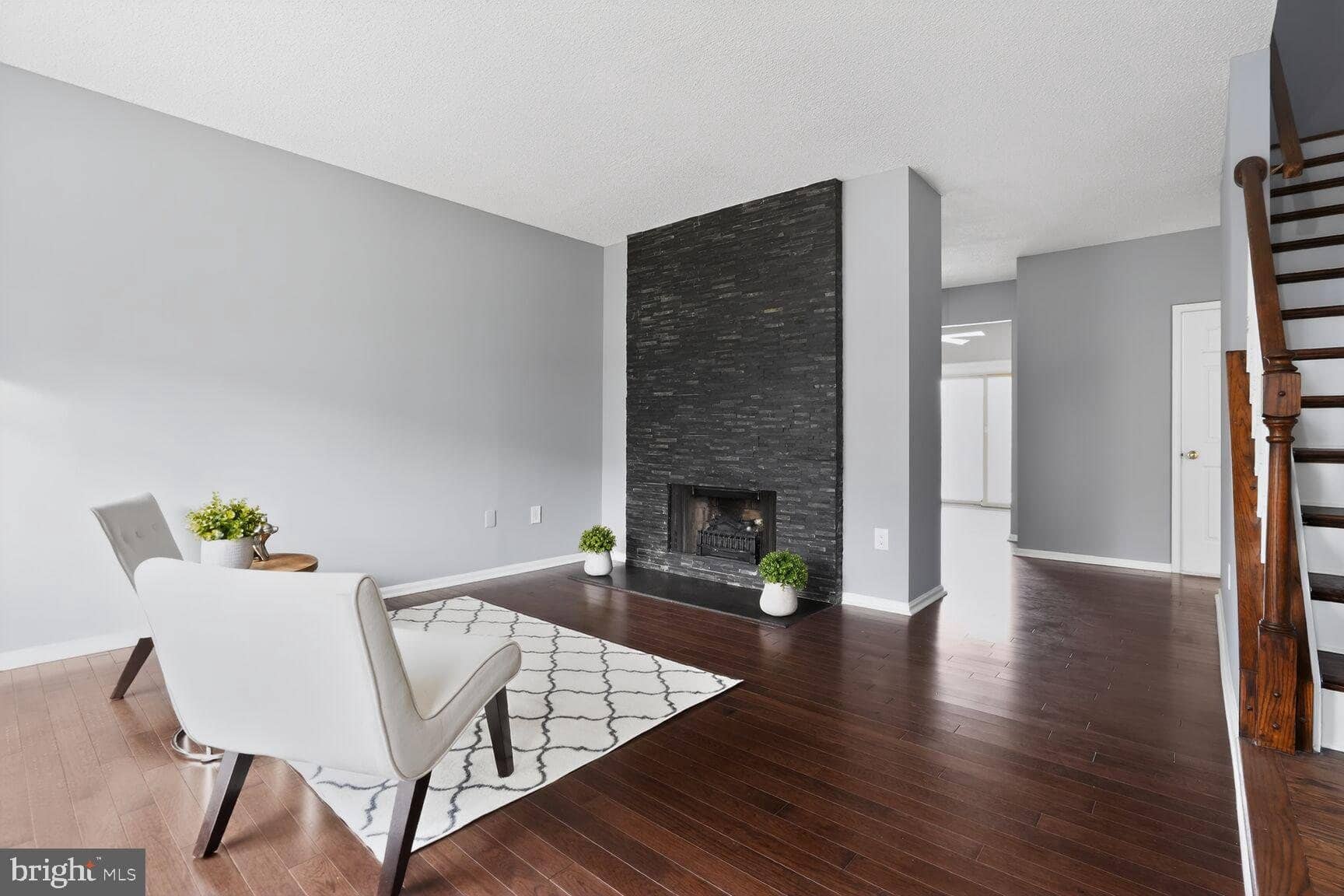 Living room with hardwood floors, a dark stacked-stone fireplace, and the staircase