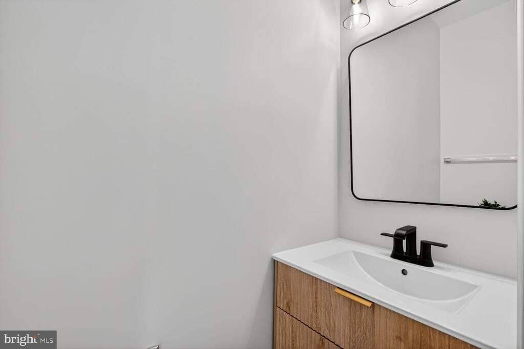 Main-level powder room with a light wood vanity, black fixtures, and a framed mirror