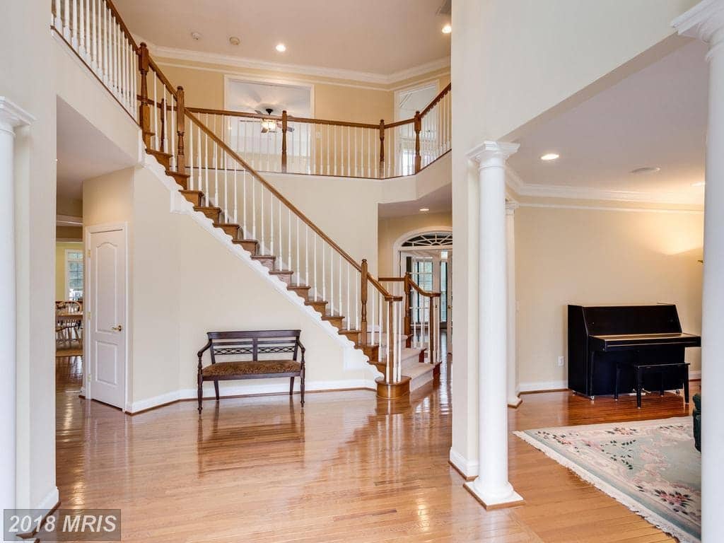 Two-story foyer at 12803 Holly Grove Court with hardwood floors, columns, and a curved dual staircase