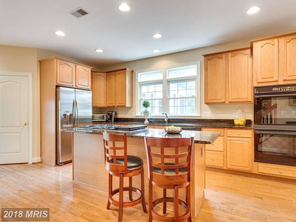 Gourmet kitchen at 12803 Holly Grove Court with warm wood cabinetry, granite counters, and stainless-steel appliances