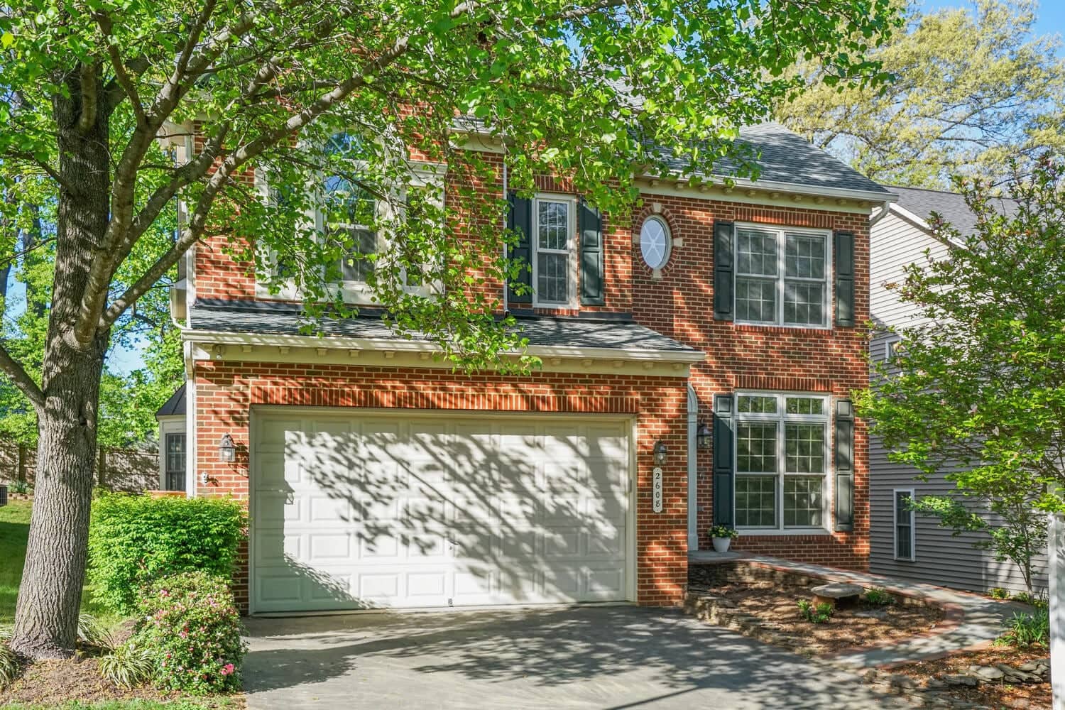 Front exterior of 2608 Amanda Court showing the brick Colonial facade, two-car garage door, and mature shade tree
