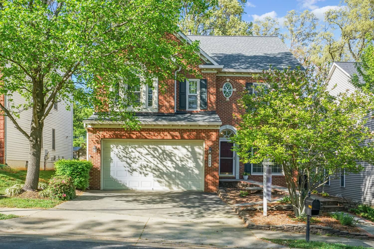 Full front view of 2608 Amanda Court with brick facade, driveway, flowering trees, and landscaped entry
