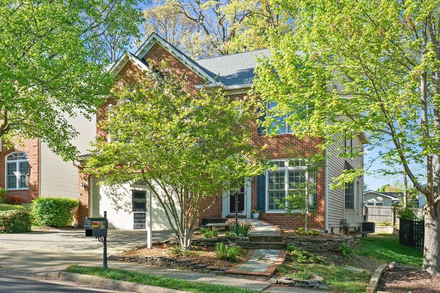 Tree-framed front exterior of 2608 Amanda Court showing the brick Colonial and stone-edged walkway