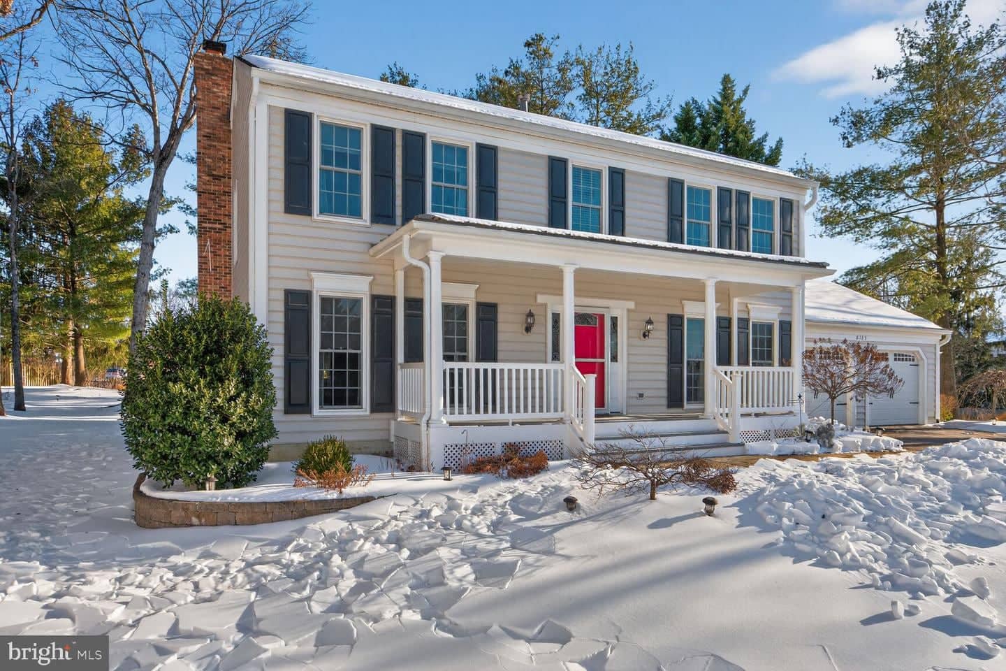 Angled winter view of the Colonial facade, covered porch, and front landscaping