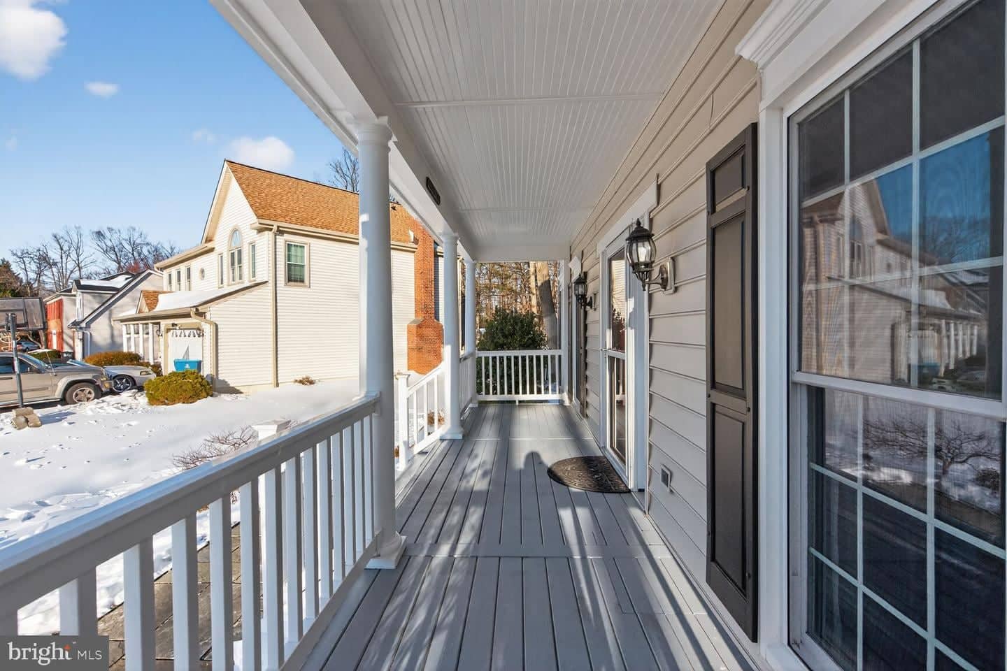 Long covered front porch with white columns, railings, and gray decking