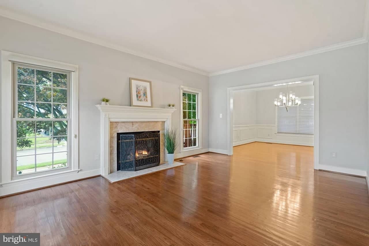 Front living room with hardwood floors, tall windows, fireplace, and opening to the dining room