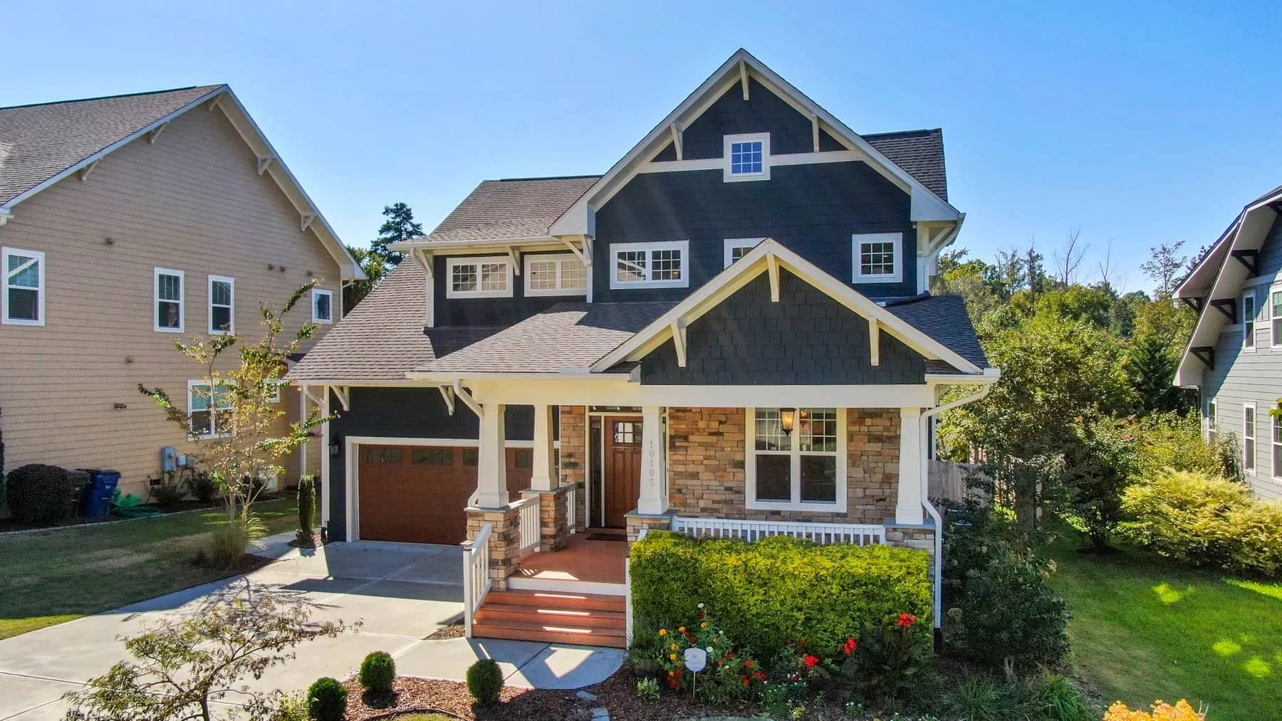 Blue Craftsman-style home with a stone porch, cream trim, and a flowering front garden — architectural inspiration