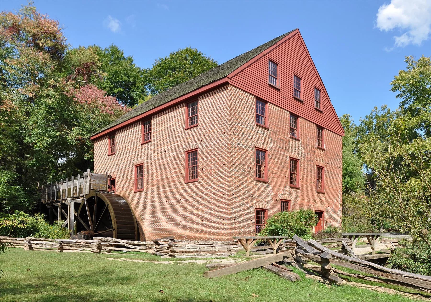 Red brick Colvin Run Mill with its waterwheel, wooden fence, and green grounds in Great Falls