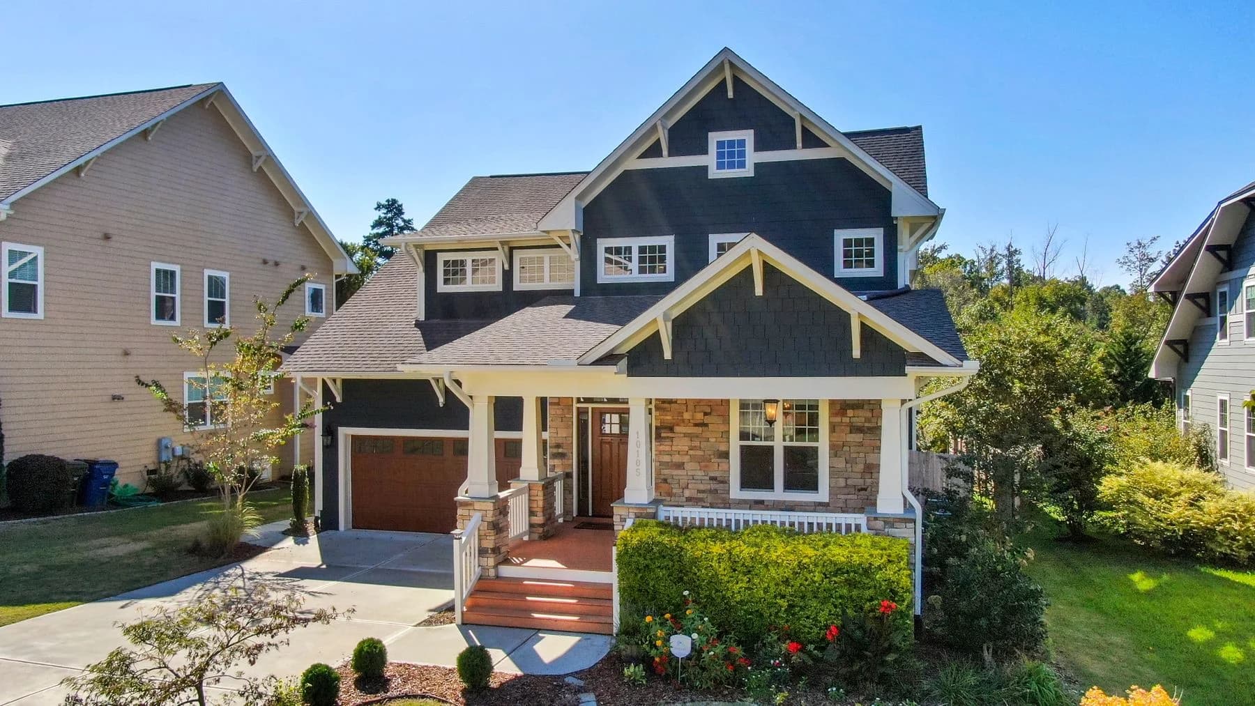 Blue Craftsman-style home with a stone porch, cream trim, and a flowering front garden — architectural inspiration