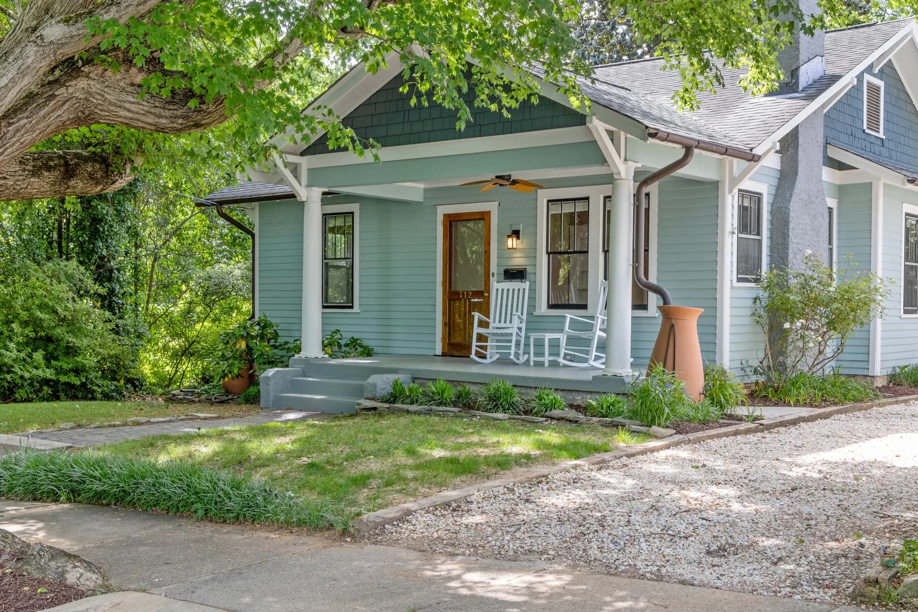 Inviting blue-gray home with a covered porch, rocking chairs, and a mature shade tree — architectural inspiration