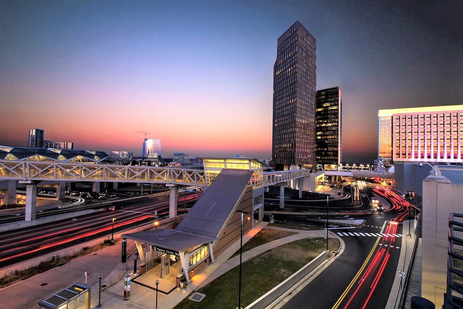 Pink and gold sunset above the Metro station canopy, pedestrian bridge, and traffic on Chain Bridge Road in Tysons