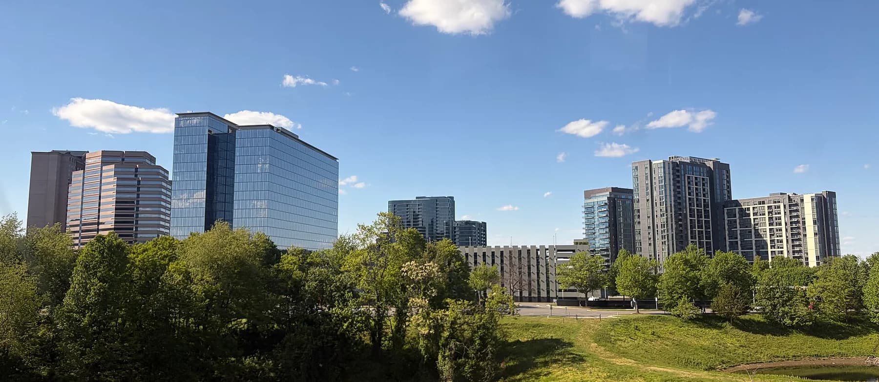 Office and residential towers above green trees and an open lawn in Tysons, Virginia