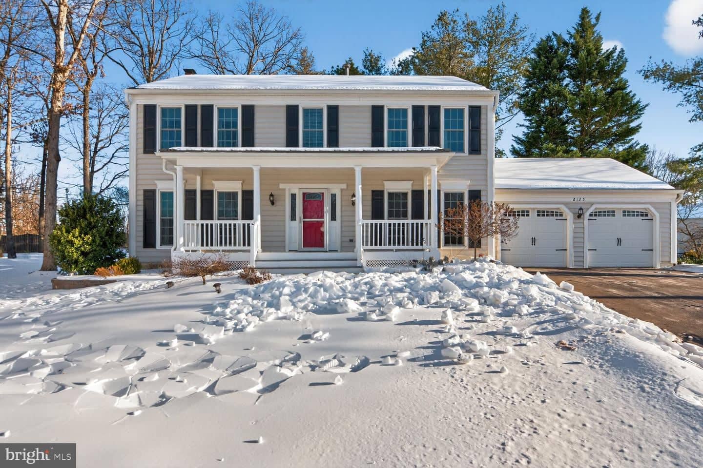 Snow-covered front exterior of 6125 Sandstone Court with full-width porch and two-car garage